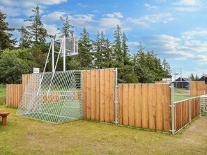 Una cancha deportiva con aro de baloncesto, rodeada por una valla de madera y una puerta de metal.