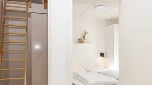 Una camera da letto con un letto, una lampada da comodino, una mensola con soprammobili e una scala in legno che conduce a un armadio.