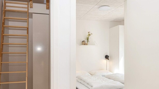 A bedroom with a bed, a bedside lamp, a shelf with decorative items, and a wooden ladder leading to a closet. - 5 Star Holiday Home in Romo (Rømø)
