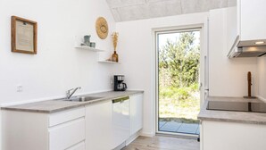 Una cucina moderna con mobili bianchi, lavastoviglie integrata, macchina da caffè e vista all'esterno tramite una porta in vetro.