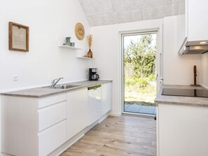 A modern kitchen with white cabinetry, a built-in dishwasher, a coffee maker, and a view of the outdoors. - 5 Star Holiday Home in Romo (Rømø)