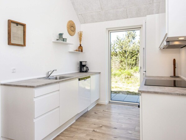 Une cuisine moderne avec des armoires blanches, un lave-vaisselle encastré, une machine à café et une vue sur l’extérieur grâce à une porte vitrée.
