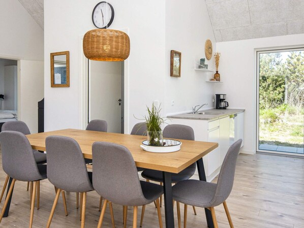 A modern kitchen with a dining area, a clock, and a view of greenery outside. - 5 Star Holiday Home in Romo (Rømø)