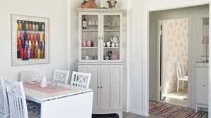 A dining area with a white table and chairs, a cabinet with glass doors, and a colorful wall art piece. - 4 Person Holiday Home in Herrljunga-by Traum (Herrljunga)