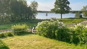 A grassy area with a wooden fence, a large tree, and a body of water in the background. - 4 Person Holiday Home in Herrljunga-by Traum (Herrljunga)