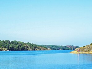 A calm lake with a clear sky, surrounded by dense green forest and rocky terrain.