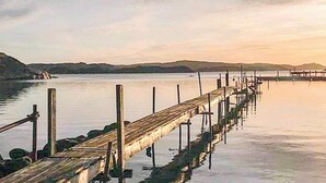 Un muelle de madera que se adentra en aguas tranquilas, con un paisaje montañoso al fondo.
