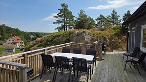 Terraza de madera con mesa y sillas, con vista a una ladera rocosa con árboles.