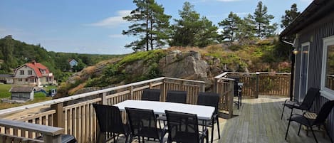 A wooden deck with a table and chairs, overlooking a rocky hillside with trees.