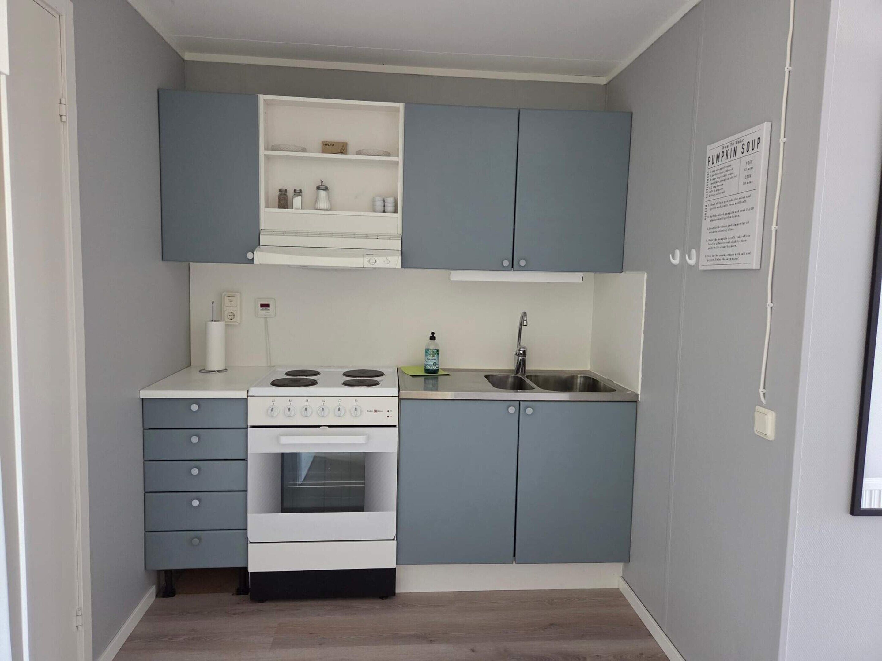 Una cocina compacta con gabinetes grises, una estufa blanca y un lavamanos.