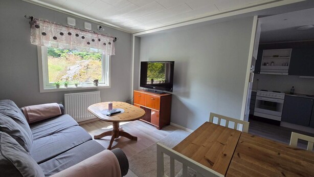 Un salón acogedor con sofá, una mesa de madera, televisión y vistas al exterior a través de una ventana.