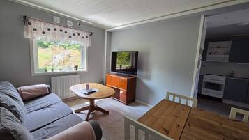 A living room with a sofa, a wooden table, a television, and a view of the outdoors through a window.