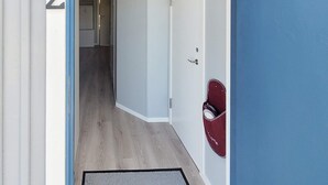 Un pasillo con una puerta marcada con el número 2, un buzón rojo y un suelo de madera.