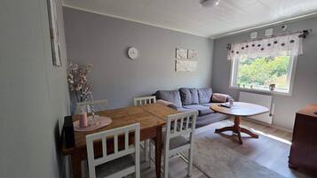 Een gezellige woonkamer met een houten eettafel, witte stoelen, een grijze bank en een kleine ronde tafel met een witte tafelkleed.