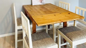 A wooden dining table with four white chairs, each with a cushioned seat.