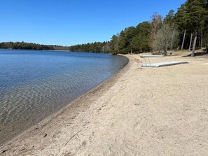 Une plage de sable fin, avec une eau claire, des arbres et une jetée.