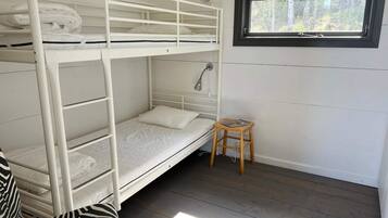 A bunk bed room with a window, a bedside lamp, and a small wooden stool.