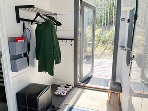 A room with a sliding glass door leading to an outdoor deck, a bench, a coat rack with a green jacket, and a storage unit with shoes. - 7 Person Holiday Home in Jarna (Järna)