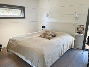 A bedroom with a bed, a nightstand, a wall-mounted lamp, and a window. - 7 Person Holiday Home in Jarna (Järna)
