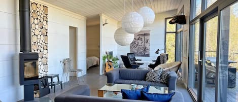 A modern living room with a wood-burning stove, a sofa, a coffee table, and a large window offering a view of the outdoors.