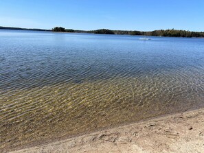 A clear lake with a sandy shore and a small boat in the distance. - 7 Person Holiday Home in Jarna (Järna)
