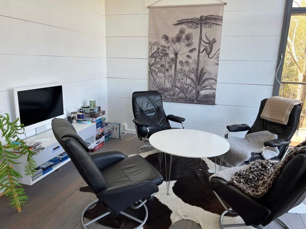 A modern room with a flat-screen TV, a round table, and four black leather chairs. - 7 Person Holiday Home in Jarna (Järna)