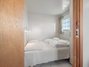 Ein kleines Zimmer mit einem Einzelbett, weißen Wänden und einer Holztür.