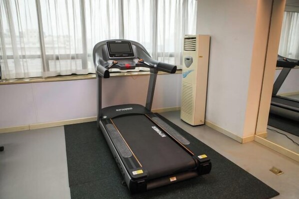 Un tapis de course dans une pièce dotée d’une grande fenêtre, d’un radiateur et d’un miroir.