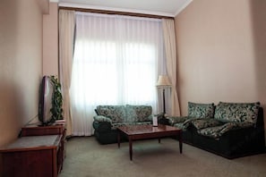 A living room with a sofa, a coffee table, a lamp, and a television on a stand. - Long Shao Heng Hotel (Beijing)