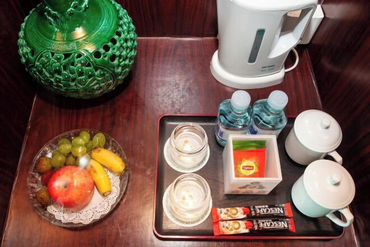 Een dienblad met fruit, een pak Nescafe, twee waterflessen, een theepot en een koffiezetapparaat op een houten tafel.