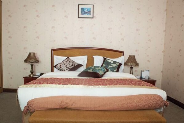 A neatly made bed with a wooden headboard, two bedside tables with lamps, and a framed picture on the wall. - Long Shao Heng Hotel (Beijing)