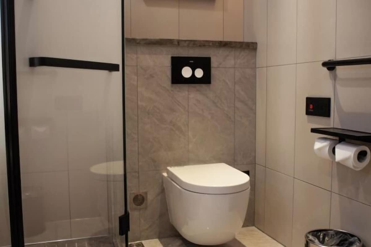 Een moderne badkamer met toilet, een glazen douchecabine en een marmeren wand.