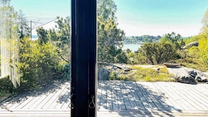 A view from a window overlooking a wooden deck with a lake and greenery in the background. - 4 Star Holiday Home in Hoviksnas (Höviksnäs)