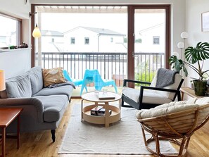 A modern living room with a grey sofa, a wicker chair, a round coffee table, and a balcony with blue chairs. - 4 Star Holiday Home in Farhult (Hoganas)