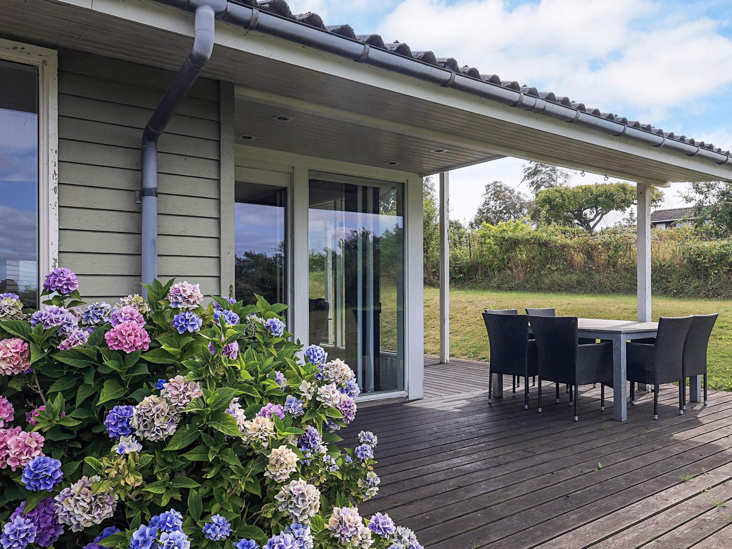 Un espacio al aire libre techado con una mesa y sillas, rodeado por un jardín de flores de hortensia.