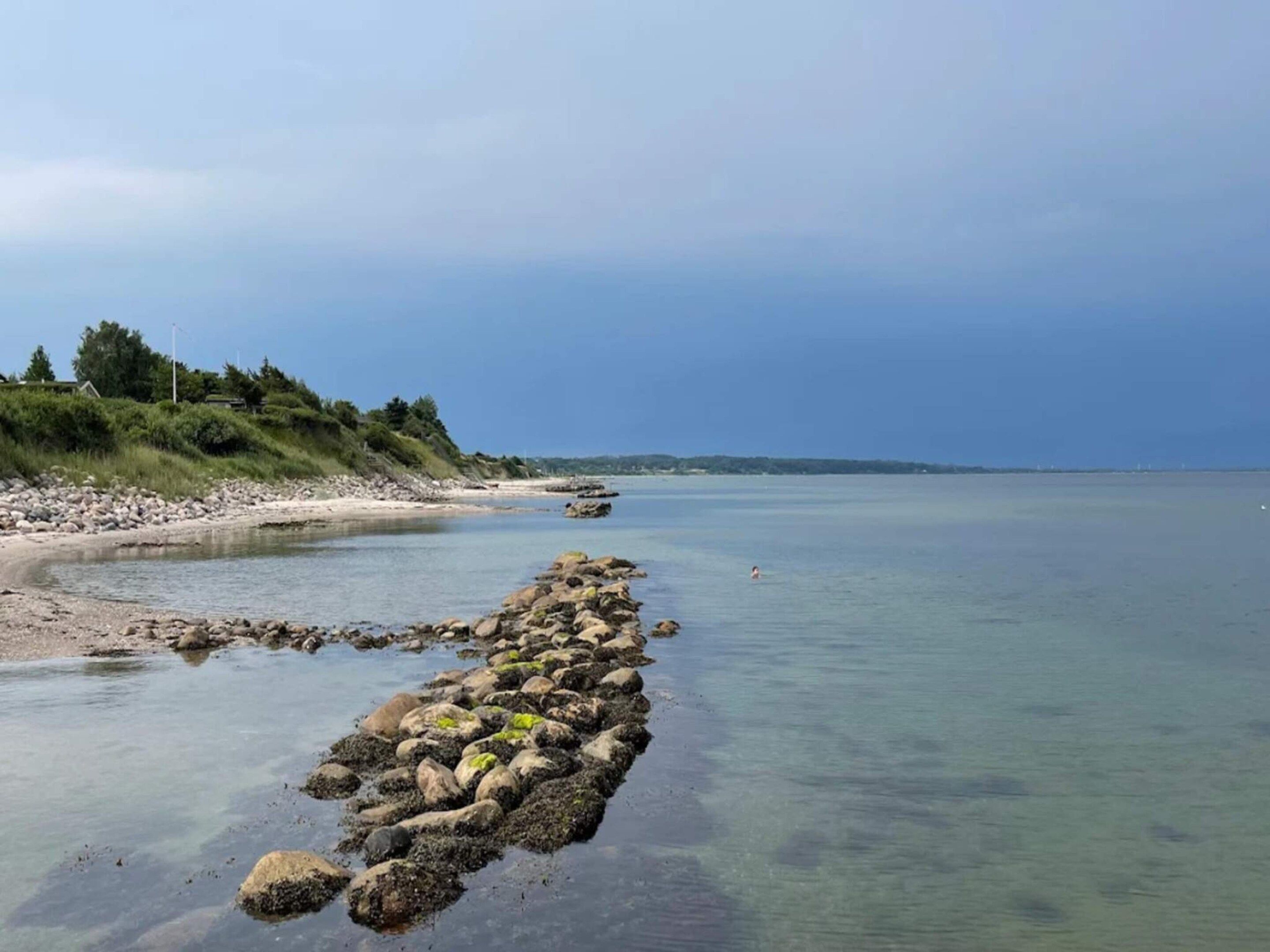 A coastal landscape with a rocky shoreline, clear water, and a distant view of land.