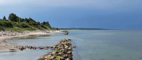 A coastal landscape with a rocky shoreline, clear water, and a distant view of land.