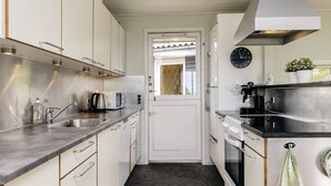 A compact kitchen with white cabinets, stainless steel appliances, a black countertop, and a visible clock on the wall. - 6 Person Holiday Home in Brenderup Fyn (Middelfart)