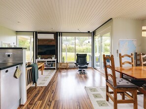 A spacious living room with a large window, a fireplace, and a dining area with wooden furniture. - 6 Person Holiday Home in Brenderup Fyn (Middelfart)