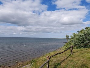 A coastal landscape with a grassy area, a wooden fence, and a view of the sea under a partly cloudy sky. - 6 Person Holiday Home in Brenderup Fyn (Middelfart)