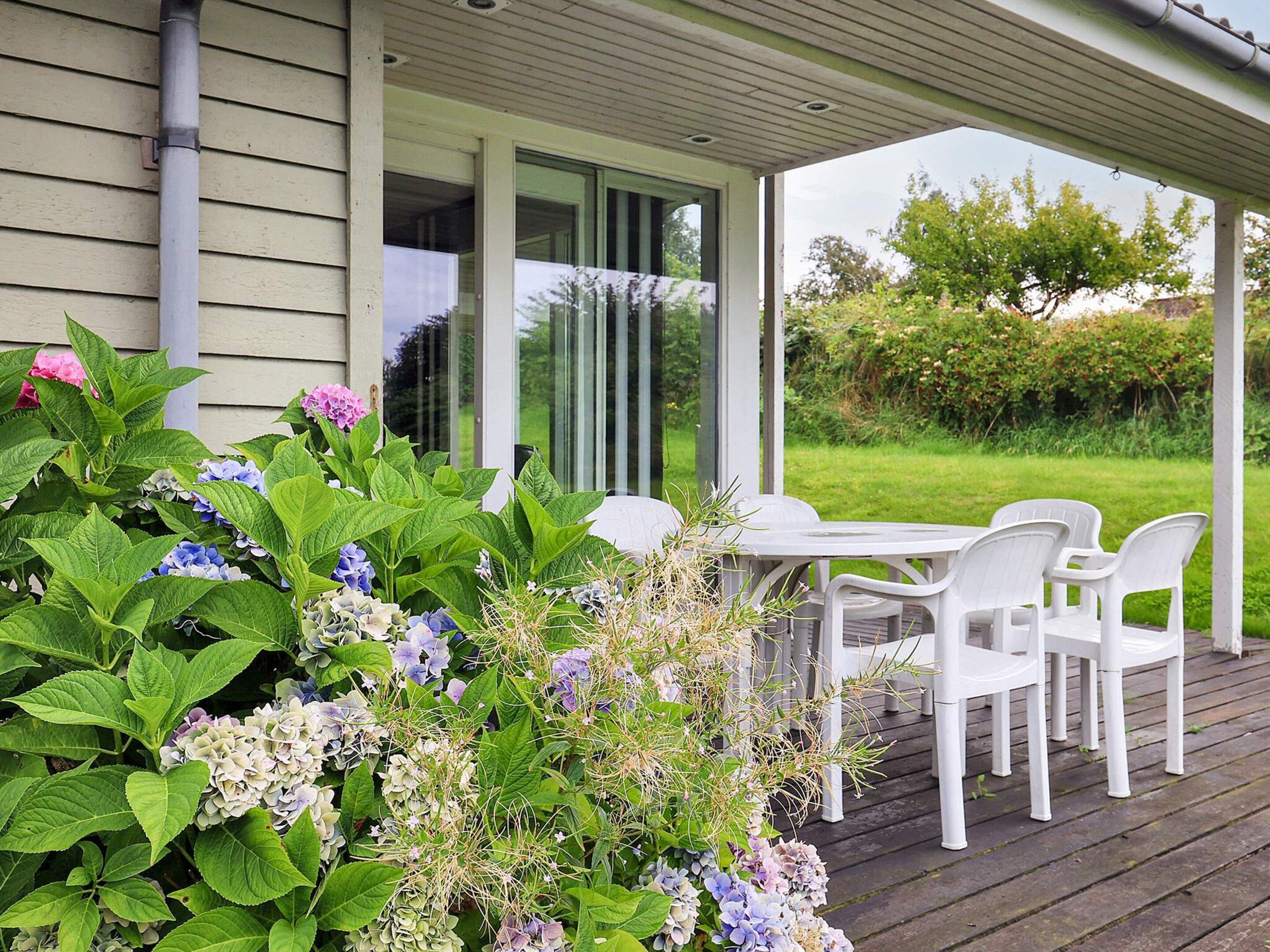 A covered outdoor seating area with a table and chairs, surrounded by lush greenery and flowers.
