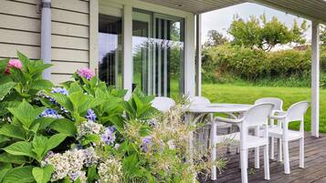 A covered outdoor seating area with a table and chairs, surrounded by lush greenery and flowers.