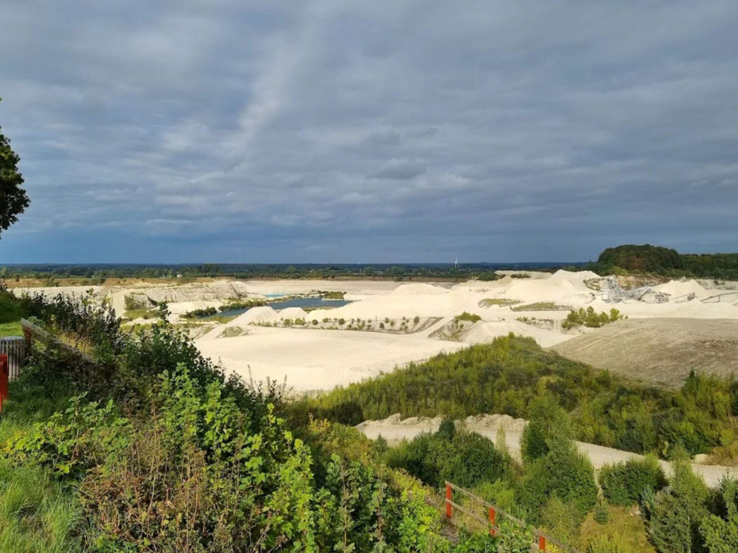 Een landschap met zandduinen, een waterpartij en een bebost gebied.