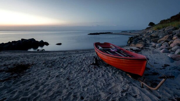 A red boat on a sandy beach with a calm sea and rocky shoreline. - 6 Person Holiday Home in Brenderup Fyn (Middelfart)