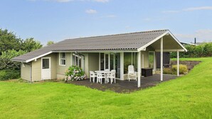 Una casa a un piano con veranda, un piccolo patio e un giardino con prato.
