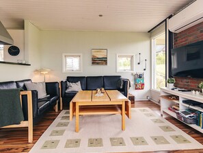 A living room with a black leather sofa, a wooden coffee table, and a television on a brick wall. - 6 Person Holiday Home in Brenderup Fyn (Middelfart)