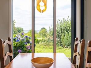 A dining table with a bowl, wooden chairs, and a view of a garden with flowers and a body of water. - 6 Person Holiday Home in Brenderup Fyn (Middelfart)