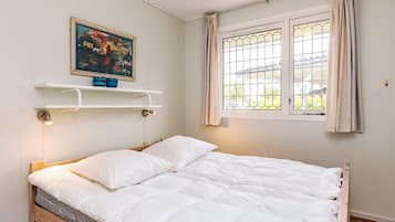 A single bed with a white duvet, a painting above it, and a window with curtains.
