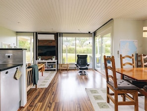 A spacious living area with a wooden floor, a dining table with chairs, a fireplace, and a large window offering a view of the outdoors. - 6 Person Holiday Home in Brenderup Fyn (Middelfart)