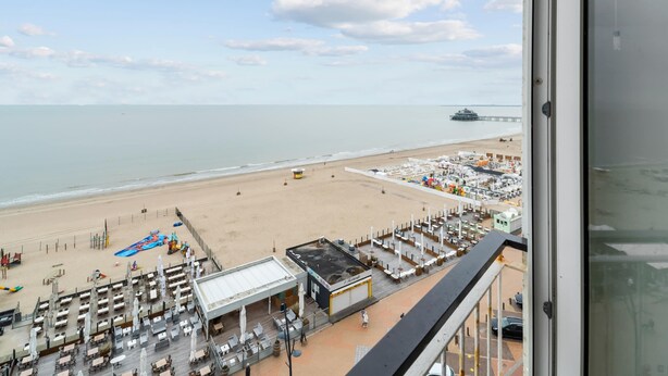 A beachside view from a balcony overlooking a beach with a pier in the distance, a lifeguard tower, and a row of beachside restaurants. - Attractive Studio With a Sea-view (Blankenberge)